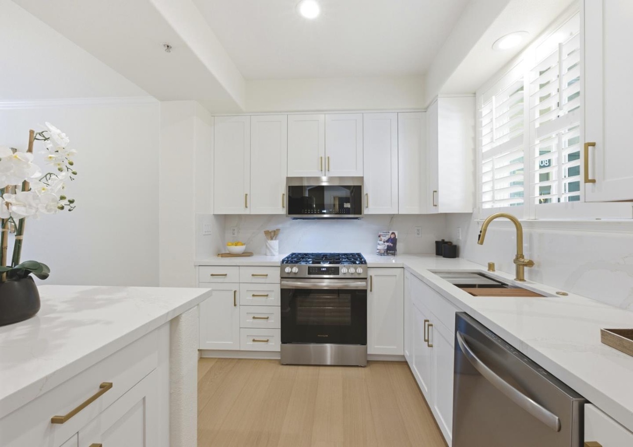 Remodeled kitchen with white shaker cabinets, quartz counters, a brass gooseberry faucet, gas range, and stainless dishwasher