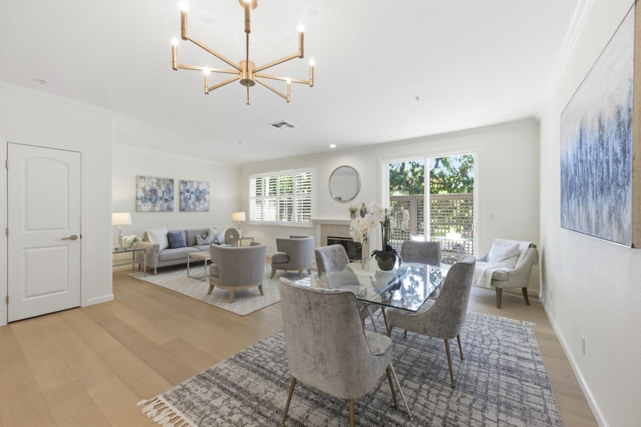 Open great room with high ceilings, a brass-arm chandelier, a tile fireplace, and a glass dining table beneath crown molding