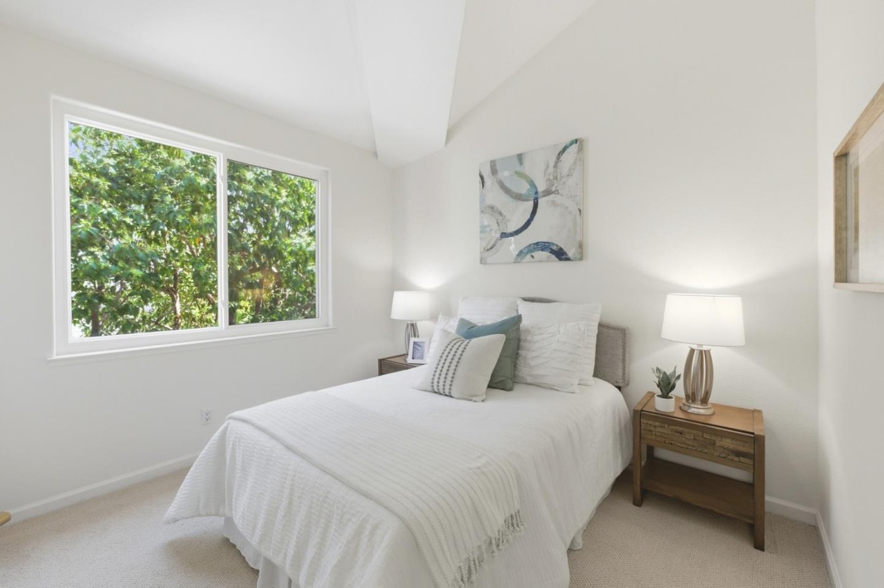 Third bedroom with a vaulted ceiling, a large window framing green treetops, and soft neutral decor