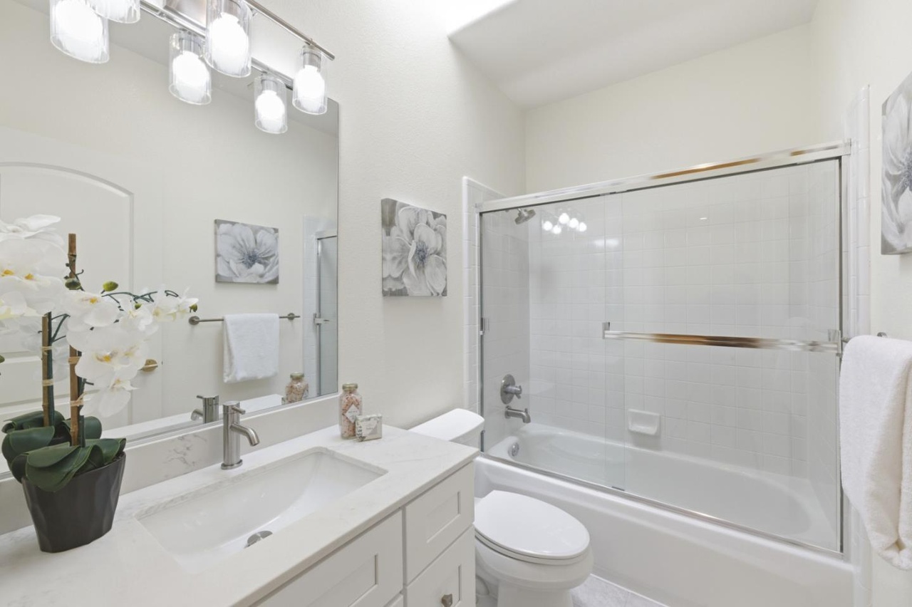 Updated bathroom with a quartz-topped vanity, framed mirror, tiled tub-and-shower, and glass enclosure